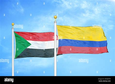 sudán y colombia dos banderas en los postes de la bandera y el cielo azul fotografía de stock