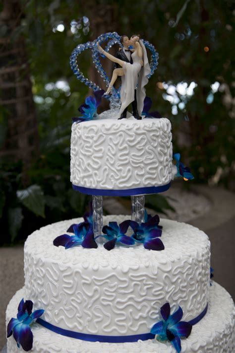 a wedding cake decorated with blue flowers and two figurines on top is shown