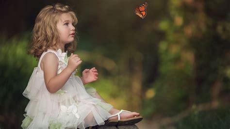 Cute Little Girl Is Sitting On Wooden Bench Seeing Butterfly Wearing