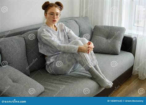 A Red Haired Girl In Pajamas And Glasses Sits On The House On The Sofa