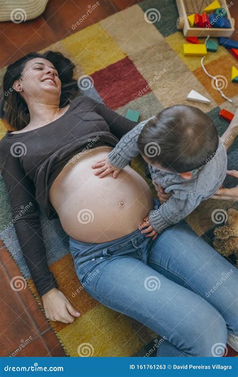 Kleinkind Das Den Bauch Seiner Schwangeren Mutter Herumträgt Stockbild