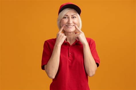Free Photo Middle Aged Blonde Delivery Woman In Red Uniform And Cap Looking At Front Making