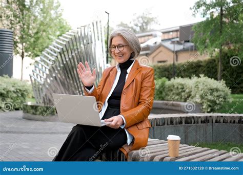 mature gray haired business woman sitting outdoors in a park have online conference with a