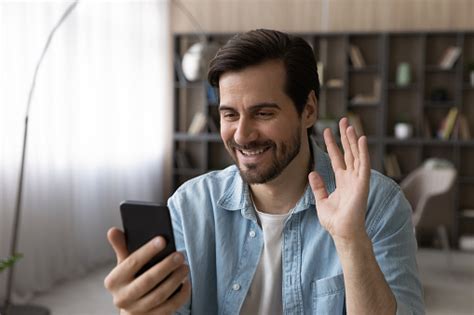 Happy Millennial Man Wave Hand Hi Look At Smartphone Screen Stock Photo