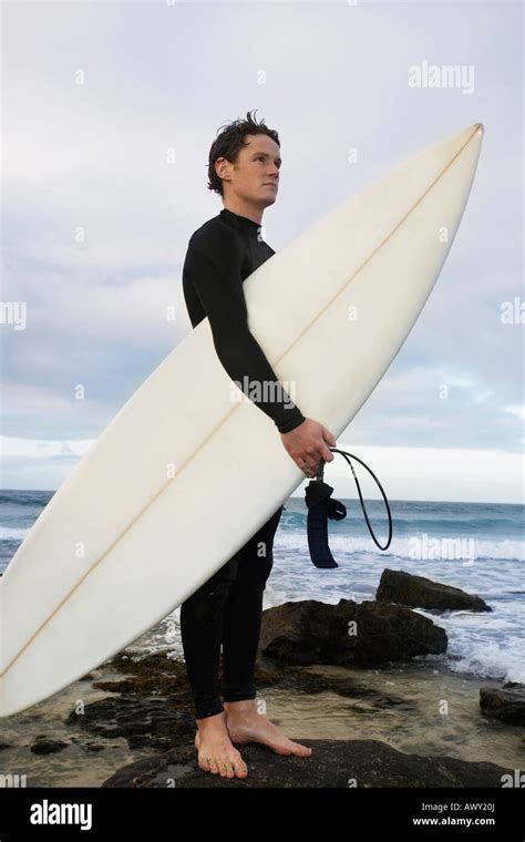 Man Holding Surfboard On Rocks On Beach Side View Stock Photo Alamy