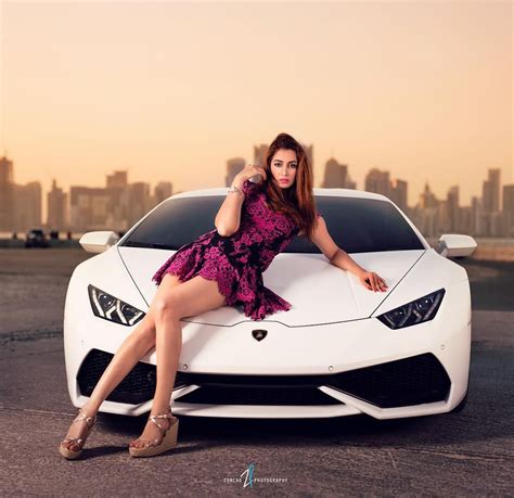 A Woman Sitting On The Hood Of A White Sports Car In Front Of A City