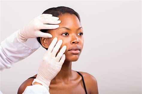 Dermatologist Checking Young African American Woman Face Skin Stock