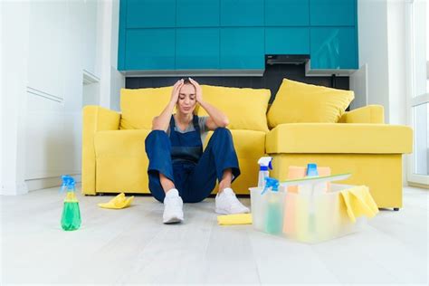 junge arbeiterin des reinigungsdienstes sitzt nahe der couch und fühlt sich müde nachdem sie