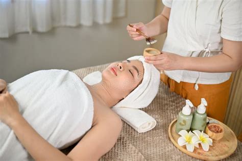 Relaxed Asian Woman Lying On Massage Table With Eyes Closed Getting Facial Treatment Stock