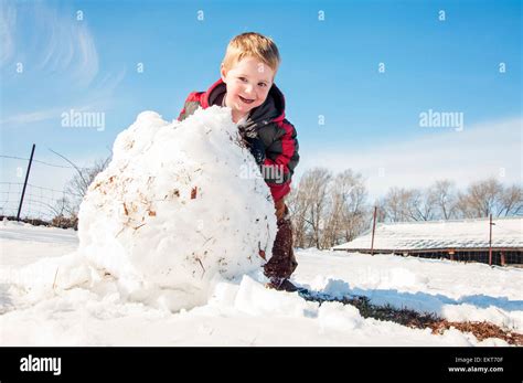 Child Rolls Large Snowball To Make Snowman Stock Photo Alamy