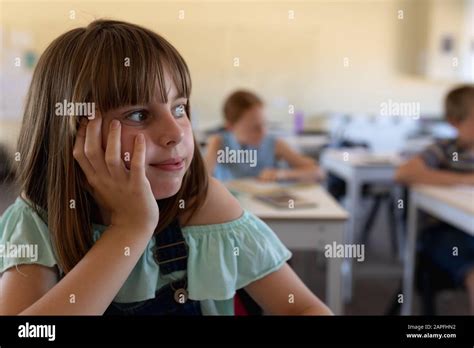 Schoolgirl Sitting At A Desk Leaning Her Head On Her Hand In An Elementary School Classroom