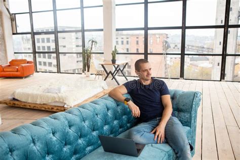 Man Sitting On Couch With Laptop And Looking In Window Stock Photo