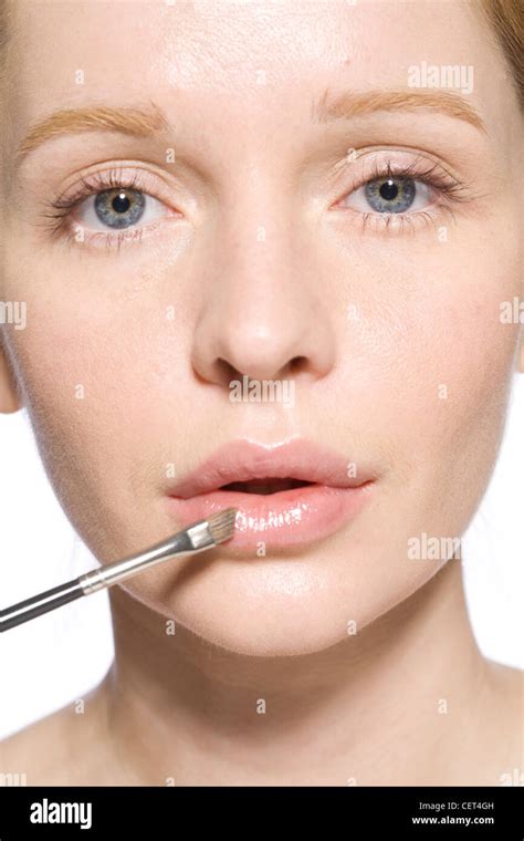 Female With Fair Hair Off Her Face Applying Pink Lipgloss To Her Bottom Lip With Make Up Brush