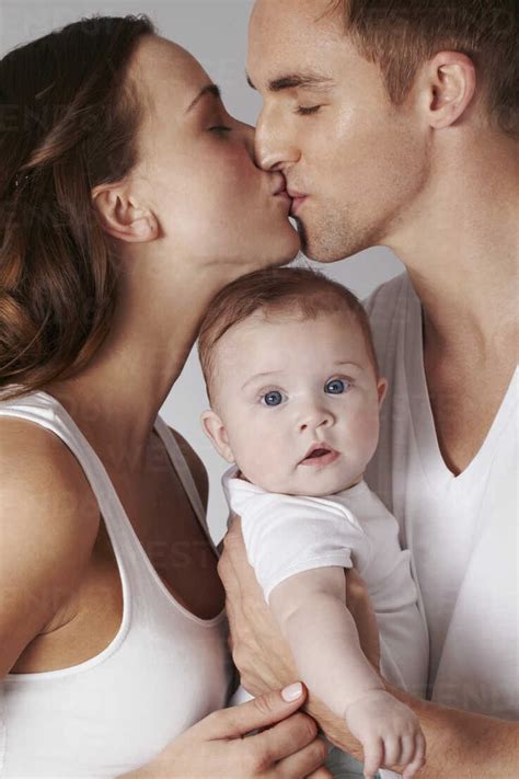 Mother And Father Kissing With Baby Daughter Stock Photo