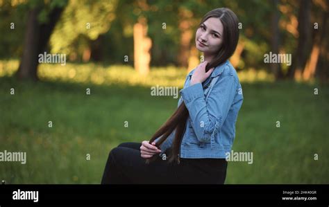 A Young Girl Strokes Her Long Hair While Sitting In The Park Stock