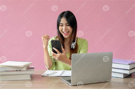 A Positive Asian Girl Is Showing Her Fist And Looking At Her Smartphone