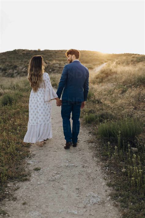 Couple Holding Hands While Walking Together During Sunset Stock Photo