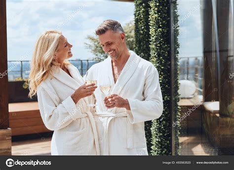 Beautiful Mature Couple In Bathrobes Enjoying Champagne While Relaxing In Luxury Hotel Outdoors