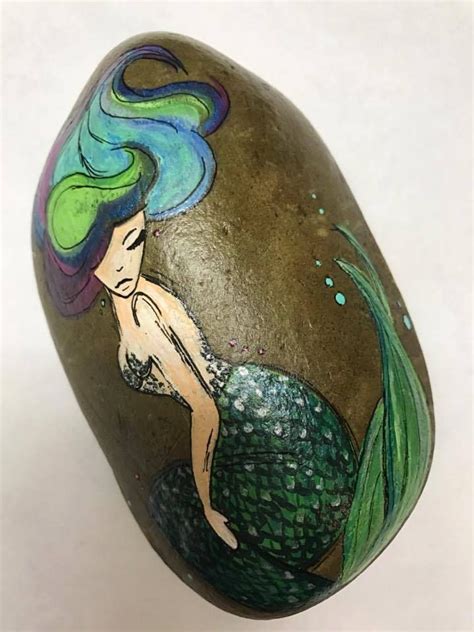 A Painted Rock With A Mermaid Sitting On It