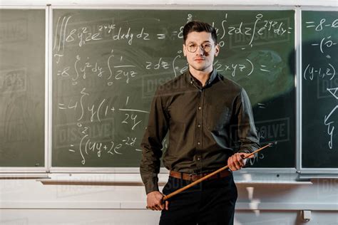 Focused Male Teacher In Formal Wear Looking At Camera And Holding