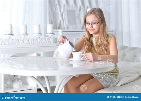 Teen Girl In Eyeglasses Sitting At White Table And Drinking Tea Stock