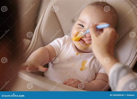Happy Baby Eating Porridge And Smiling In High Chair Stock Photo