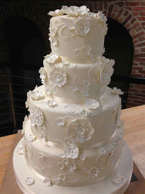 a three tiered white wedding cake sitting on top of a wooden table next to a brick wall