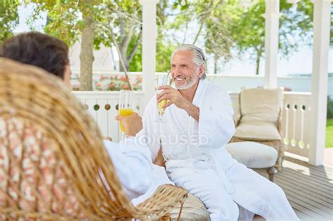 mature couple in spa bathrobes drinking mimosas in resort gazebo — outdoors romance stock