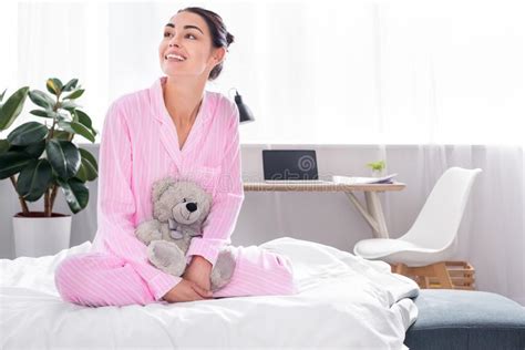 Cheerful Woman In Pink Pajamas With Teddy Bear Sitting On Bed Stock