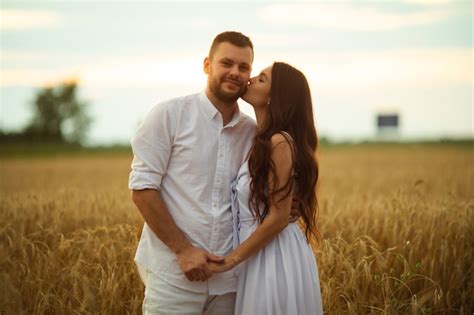 저녁 일몰 동안 밀밭에 그녀의 뒤에 서 있는 동안 그녀의 예쁜 아내를 포옹 하는 웃는 남자 사랑 개념 무료 사진