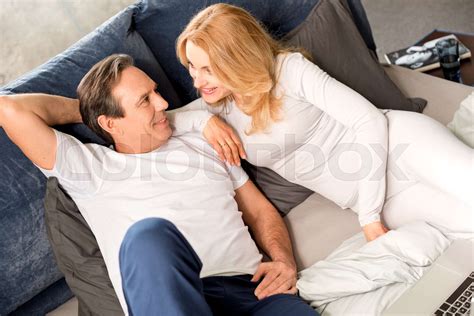 happy middle aged couple looking at each other and lying on bed at home stock image colourbox