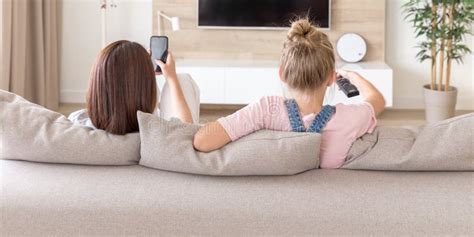 Mother And Daughter Sitting On Couch Watching Tv In Living Room Stock