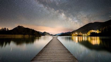 Pier Mountains Reflection On Lake Under Starry Cloudy Sky House With