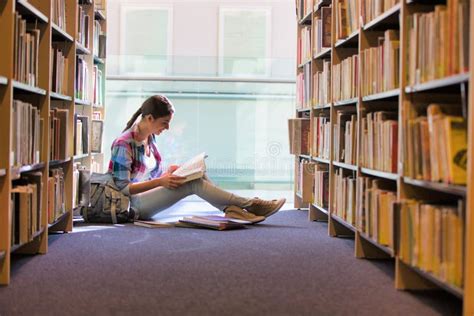 Student Reading Book While Sitting Against Bookshelf At Library Stock