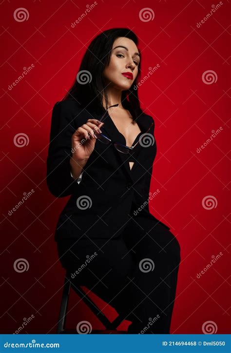 gorgeous arrogant adult woman in official pantsuit with deep neckline sits posing holding