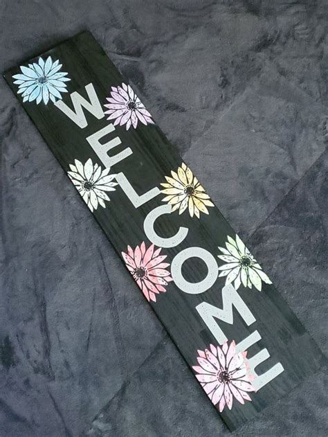 A Welcome Sign With Flowers Painted On It Sitting On Top Of A Gray