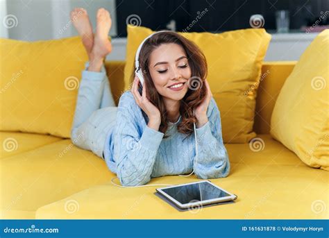 Satisfied Happy Girl Using Tablet While Lying On Comfortable Yellow Sofa And Enjoying Pleasant