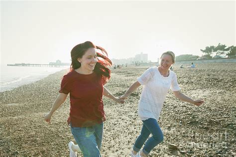 Playful Lesbian Couple Running On Beach Photograph By Caia Image