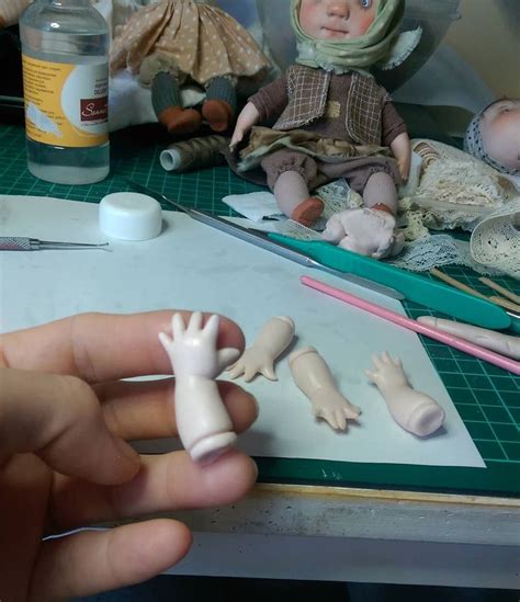 A Person Holding A Doll In Their Hand Next To Other Dolls On A Table With Scissors And Glue