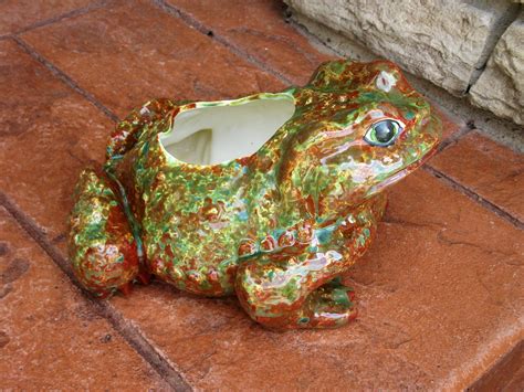 A Ceramic Frog Planter Sitting On Top Of A Red Brick Floor Next To A