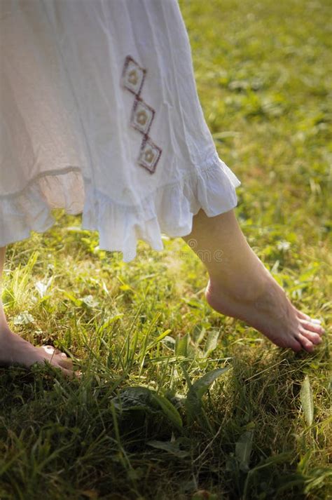 Close Up Of Barefoot Woman In White Dress Is Walking On The Grass Stock