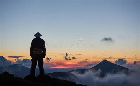 Man Standing On A Ledge Of A Mountain Enjoying The Beautiful Sunset