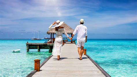 a happy couple in white summer clothing on vacation walks along a wooden pier over tropical