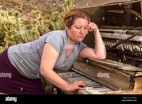 Mature Woman In Desert Setting Playing A Wooden Antique Piano With A Sad Contemplative