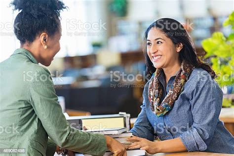 Friendly Hispanic Librarian Is Assisting Adult Student In College