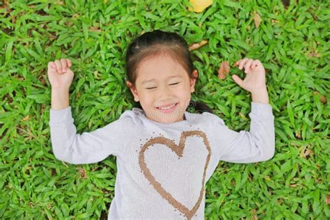 Happy Cute Little Asian Child Girl Lying On Green Lawn Smiling And