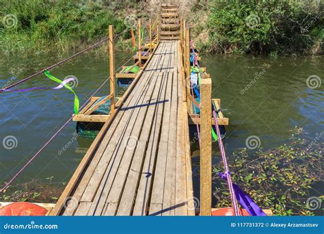 Old Wooden Pontoon Bridge With Rope Rails On A Small Quiet River Stock
