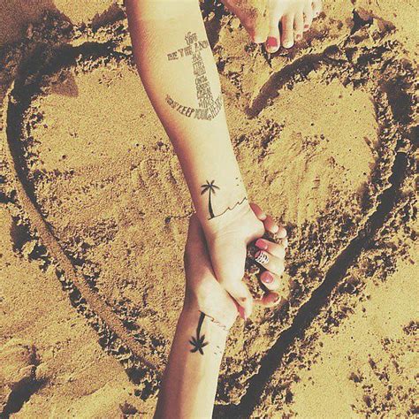 Two People Holding Hands In The Sand With A Heart And Anchor Tattoo On