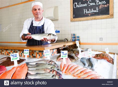 Fishmonger Behind Counter In Shop Holding Out Fish Portrait