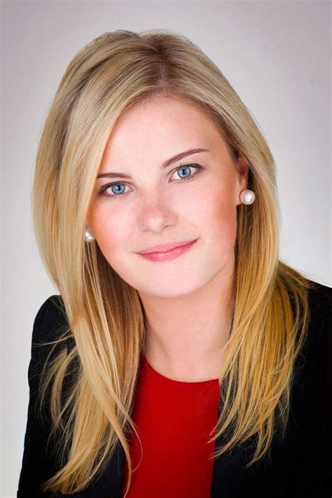 A Woman With Blonde Hair And Blue Eyes Wearing A Black Blazer Red